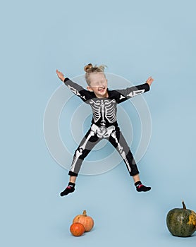 Little boy in skeleton costume jumping in the air with his eyes closed over blue