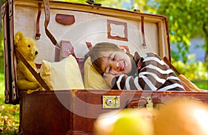 Little boy sleeps in a large suitcase in the autumn park