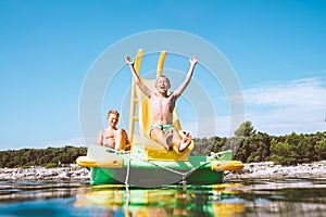 Little boy sliding down into sea water from floating Playground slide Catamaran as she enjoying sea trip with his brother
