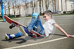 Little boy slipped and fell off the skateboard on the asphalt of the playground