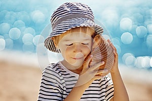 Little boy smiling at the beach in hat andholding shell