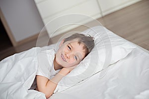 Little boy smiling during waking up in white bed