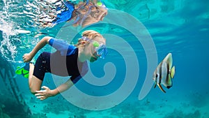 Little boy in snorkeling mask dive underwater with tropical fishes