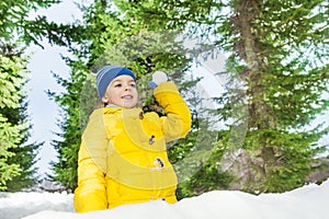 Little boy with snowball in park behind the wall