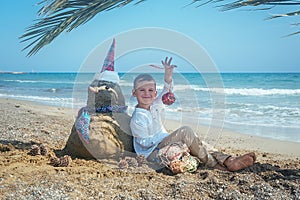 Little boy and Snowmen at tropical ocean beach in santa hat. New Years and Christmas holiday in hot countries concept