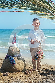 Little boy and Snowmen at tropical ocean beach in santa hat. New Years and Christmas holiday in hot countries concept
