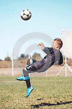 Little boy with soccer ball doing flying kick at stadium