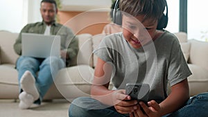 Little boy son playing video game on mobile phone in headphones on floor happy multiracial family using diverse devices