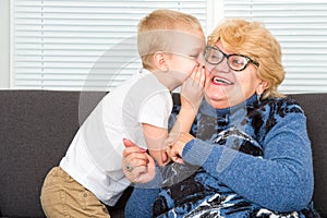 A little boy speaks the secret of his beloved grandmother in the ear.