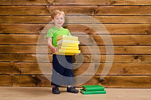 Little boy with stack of books at wooden wall