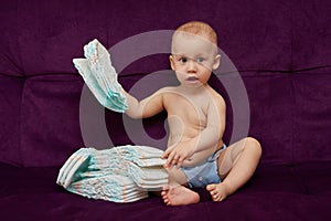 Little boy with stack of diapers or nappies on purple background