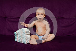 Little boy with stack of diapers or nappies on purple background