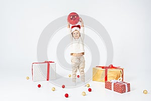 Little boy standing between gifts and holding big red Christmas ball in hands. Isolated on white background. Holidays, christmas,