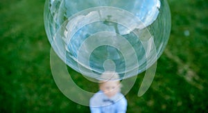 Little boy standing on the grass blurred looks from the bottom up at the big bubble with a reflection