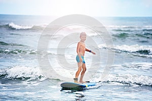 Little boy standing on surf board in the water