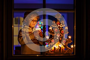 Little boy standing by winter at Christmas time and holding candle