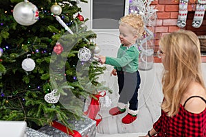 A little boy stands by the Christmas tree and looks at the Christmas decorations