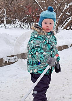 A little boy stands with a hockey stick in winter in a snowy park
