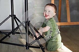 The little boy stands relying on the rack of the lighting unit.