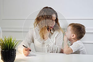 Little boy is stopping his mom to work while she is calling phone in her workplace in office. Working mother.