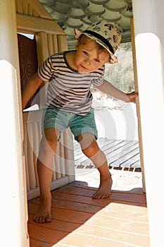 A little boy in a striped shirt in a small plastic playhouse on the beach