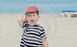 Little boy in a striped T-shirt whimsical cries against the sea.