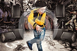 The little boy in the style of Hip-Hop . Children`s fashion.Cap and jacket. The Young Rapper.Graffiti on the walls.Cool rap dj.