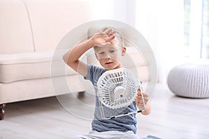 Little boy suffering from heat in front of fan