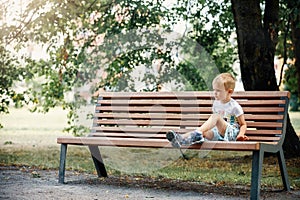 Little boy in summer city Park sitting on a bench
