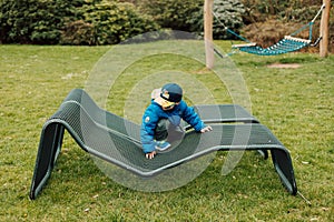 A little boy in sunglasses crawls on a park bench