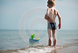 Little boy in sunglasses playing with toy boat