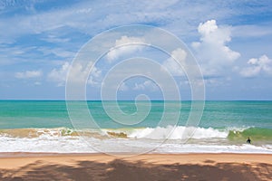 Little boy surfing in the blue sea in sunny day. White sand beach foregrounds, clouds and light blue sky backgrounds. Summer