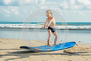 Little boy surfing on tropical beach. Child on surf board on ocean wave. Active water sports for kids. Kid swimming with