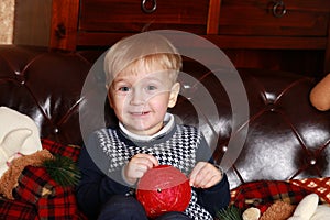 A little boy in a sweater sitting on a brown sofa