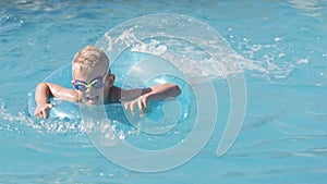 Little boy in swimming pool, child having fun, sitting on blue swimming ring, playing under water. Summer travel family