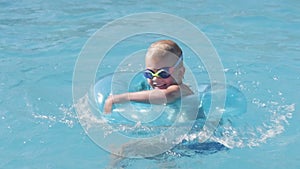 Little boy in swimming pool, child having fun, sitting on blue swimming ring, playing under water. Summer travel family