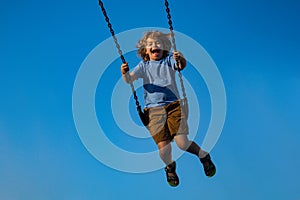 Little boy swinging on chain swing on city kids playground. Swing ride. Cute child having fun on a swing on summer sky