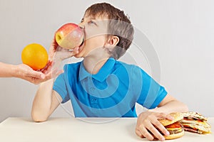 Little boy at the table chooses between fastfood and healthy diet on white background