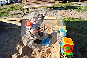 A little boy of three years old is playing on a cool spring sunny day in the sandbox in the city yard with his toy truck