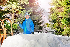 Little boy throw snowball hiding behind snow wall