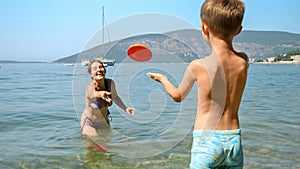 little boy throwing frisbee to his mother standing in the sea next to the beach. Family holiday, vacation and fun