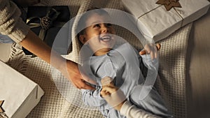 Little boy is tickled while he lies on the floor under the Christmas tree in slow motion