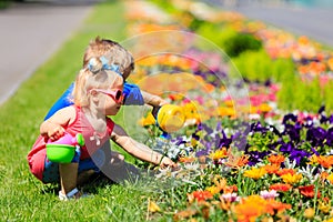 Little boy and toddler girl watering flowers in summer