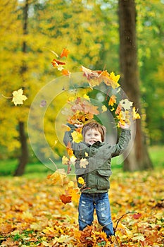 Little boy tossing leaves in autumn park