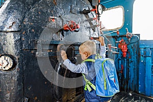 Little boy tourist considers controls Old black steam locomotive in Russia, Moscow railway station