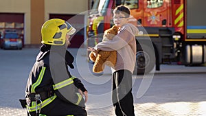 Little boy with a toy and firefighter in protective uniform in fire station