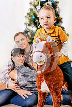 Little boy on toy horse with his parents under the Chrismas tree