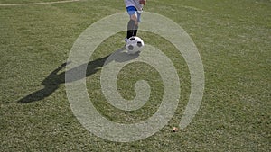 A little boy trains on the football field, practicing dribbling and feints.