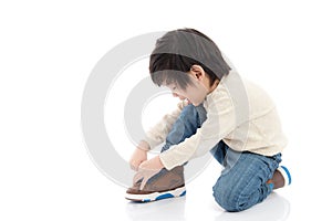 Little boy tying his shoes in white