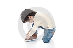 Little boy tying his shoes in white